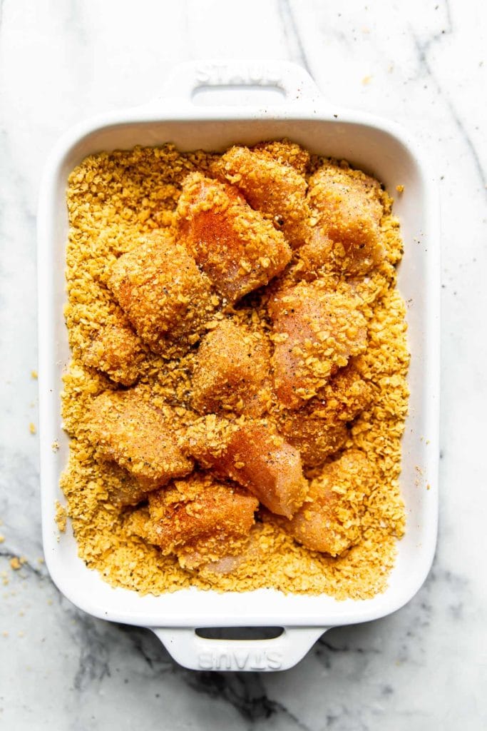 Overhead view chicken pieces in crushed corn tortilla chip mixture for a breading for homemade chicken nuggets