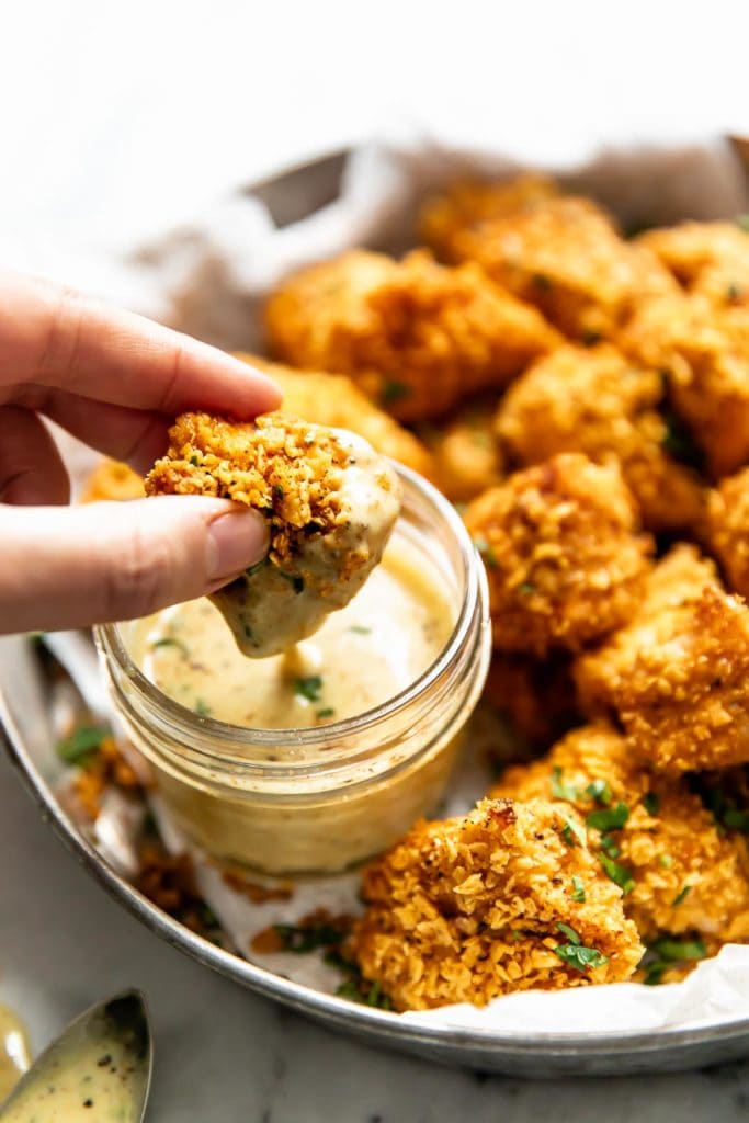 A homemade chicken nugget being dipped in small jar of honey mustard sauce