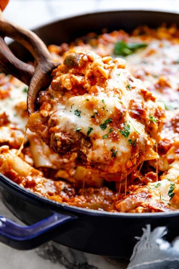 A wooden serving spoon scooping a hefty portion of easy cheesy skillet lasagna out of a cast iron skillet