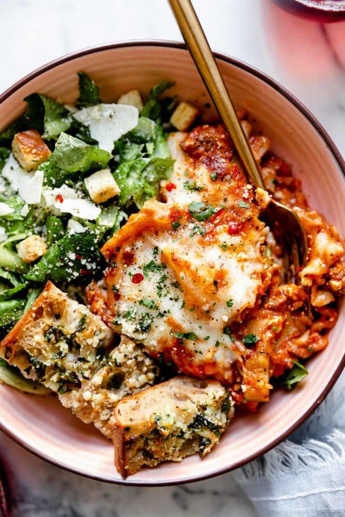 Overhead view of Easy Skillet Lasagna plated in a shallow bowl with Caesar salad on the side and shaved parmesan sprinkled on top.