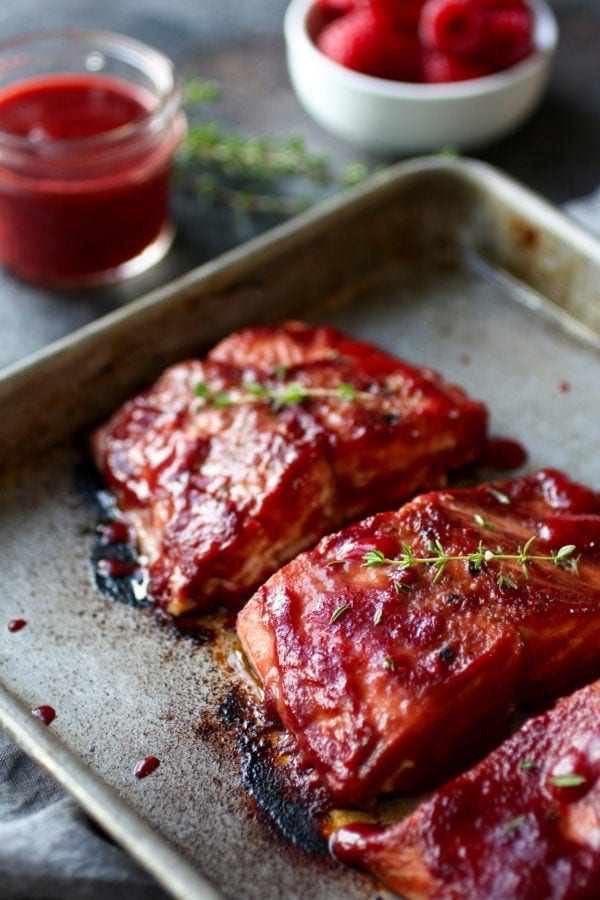 Raspberry glazed salmon fillets on a baking sheet garnished with fresh thyme.