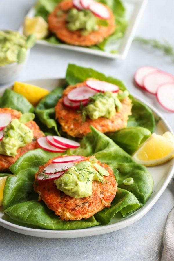 Three salmon burgers on leaf lettuce 'buns' topped with avocado sauce, green onion, and sliced radishes