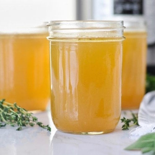 Three jars of Instant Pot Bone Broth with fresh herbs around them