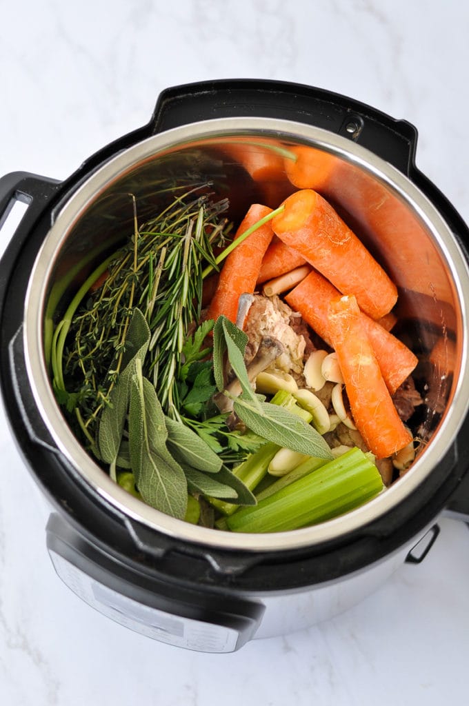 Roughly chopped root vegetables, fresh herbs, chicken bones, and garlic in an Instant Pot ready to make bone broth