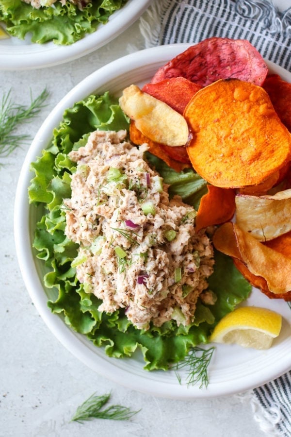 Quick and easy salmon salad served on a bed of lettuce with sweet potato chips and a lemon wedge on the side