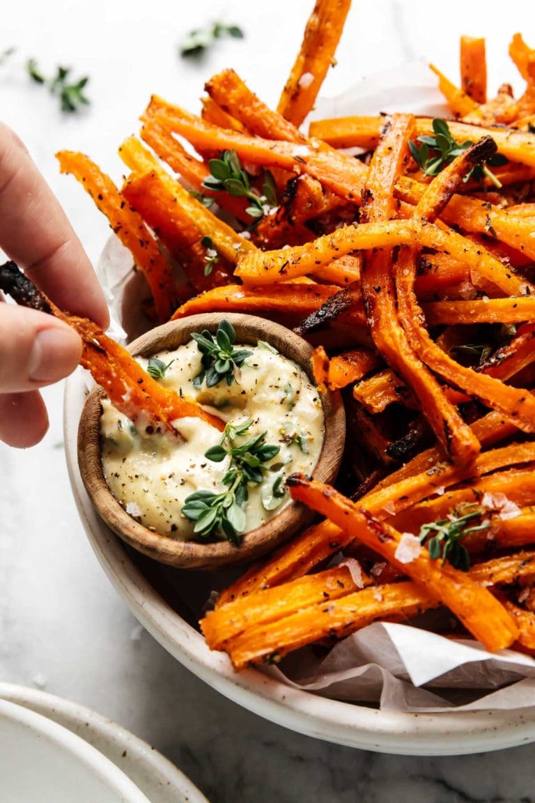 Close up view of a plate filled with carrot fries and a small bowl of aioli sauce for dipping.