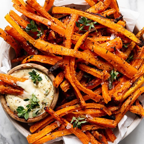 A large bowl of oven baked carrot fries with a side of dijon-thyme aioli