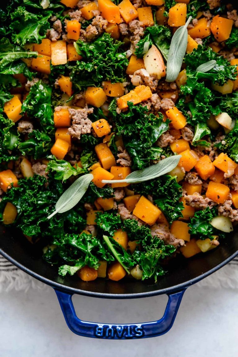 A pan of butternut squash and apple hash with sausage topped with fresh sage leaves. 