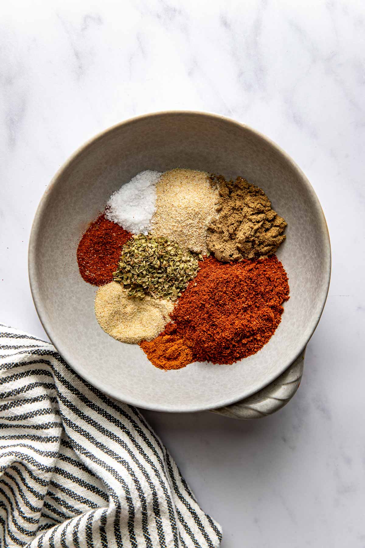 Overhead view of a ceramic bowl filled with different piles of seasonings ready to be mixed into Homemade Taco Seasoning. 
