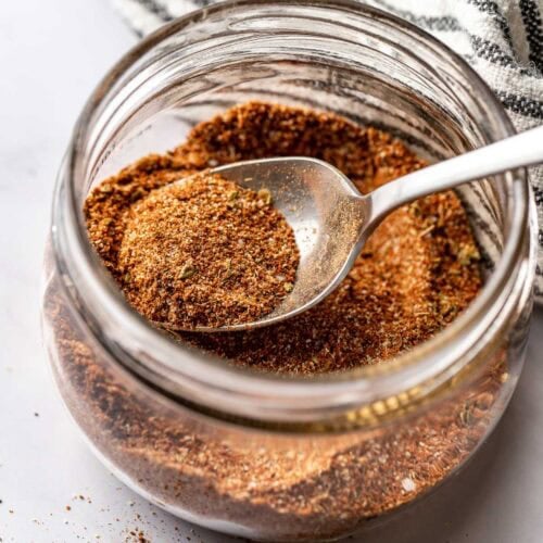 Close up view of a small mason jar filled with Homemade Taco Seasoning and a spoon in the jar to show texture.