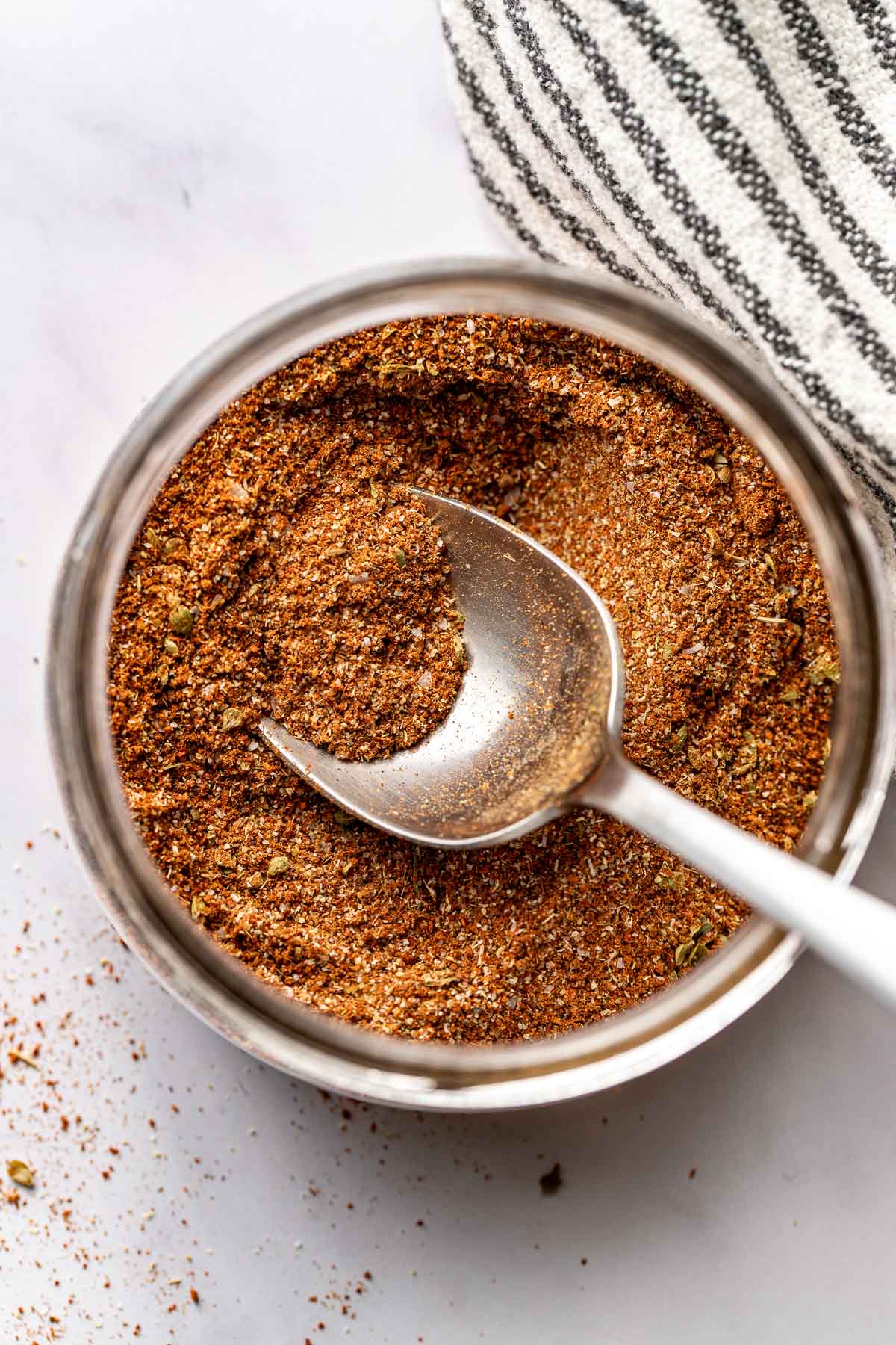 Overhead view of a small glass mason jar filled with Homemade Taco Seasoning and a spoon in the spices. 