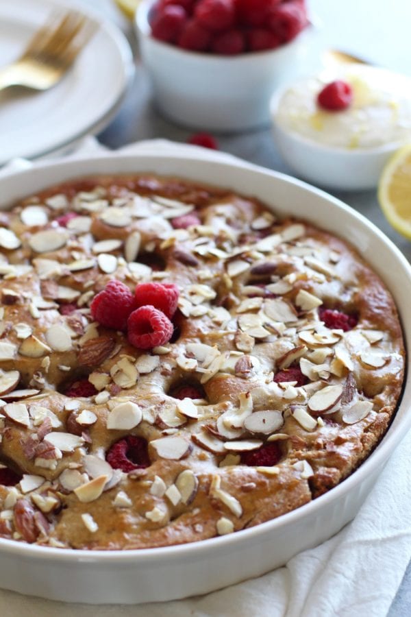 Raspberry Coffee Cake in a white pie plate topped with slivered almonds and fresh raspberries