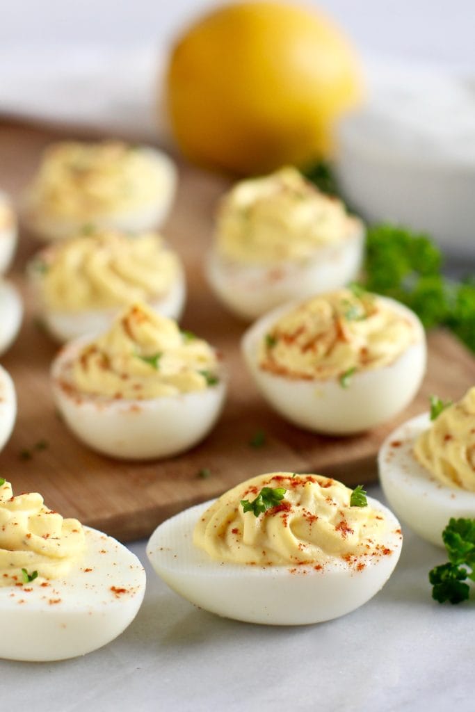 Several Greek yogurt deviled eggs on a cutting board topped with paprika and fresh herbs.