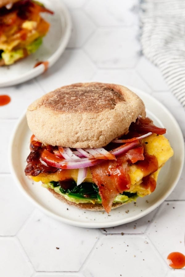 A breakfast sandwich in an English muffin with egg, bacon, cheese, and onion plated on a small plate.