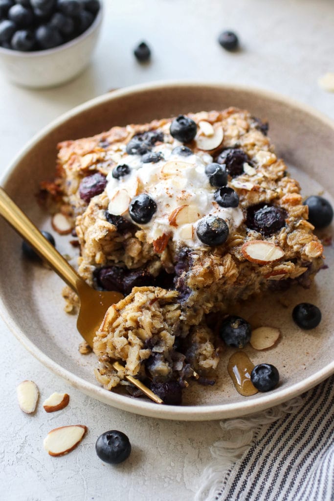 Blueberry baked oatmeal in a shallow bowl with a forkful on creamy baked oatmeal on a gold fork