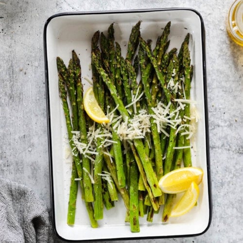 Fresh grilled asparagus in a grill pan topped with fresh parmesan and lemon wedges
