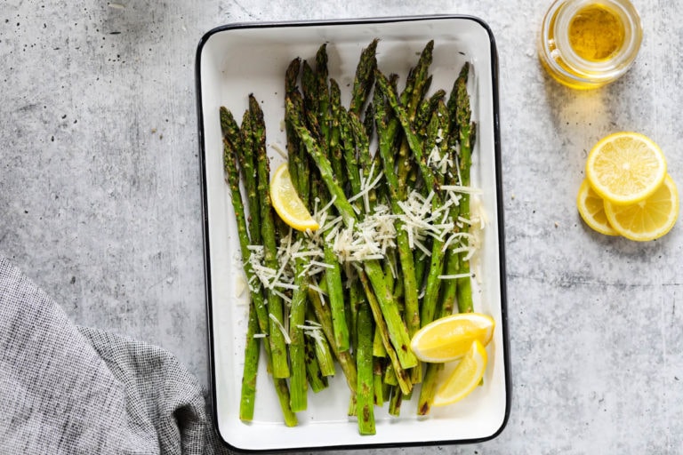 Grilled asparagus spears in metal tray sprinkled with fresh parmesan cheese and lemon wedges