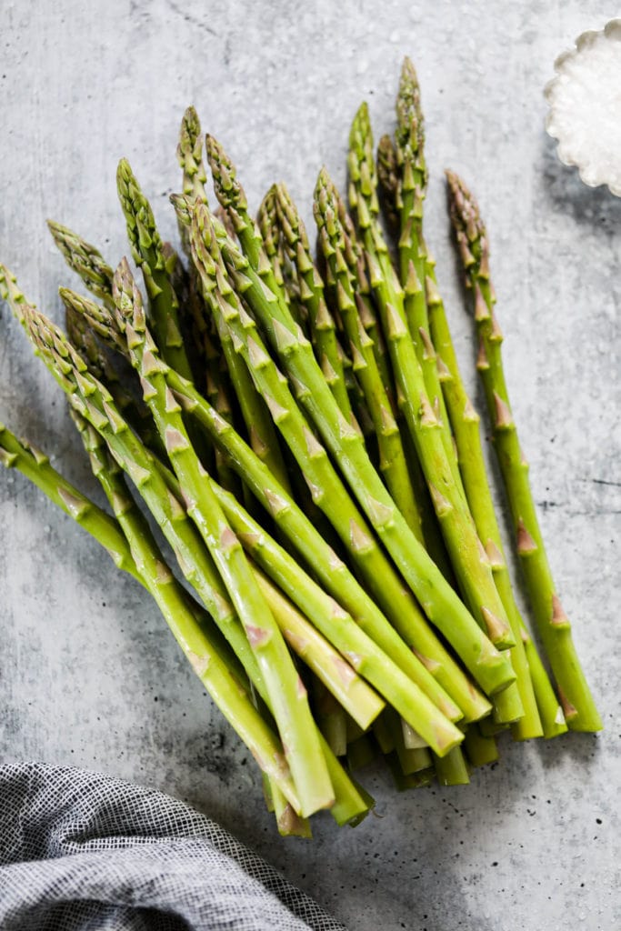 Fresh asparagus stalks on gray background next to a small dish of flakey sea salt. 