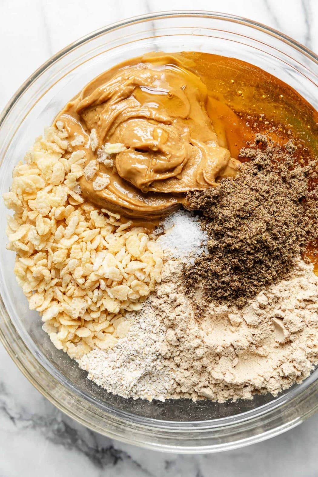 All ingredients for mini peanut butter protein bars in a glass mixing bowl ready to be mixed together.