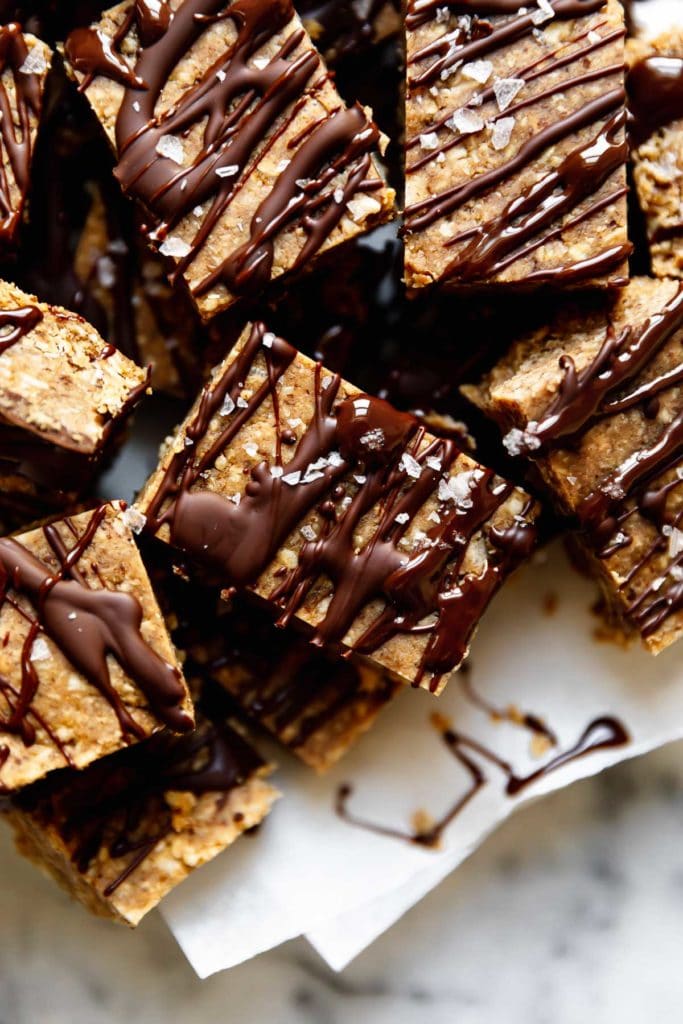 A close up view of mini peanut butter bars drizzled with dark chocolate and sprinkled with sea salt flakes.