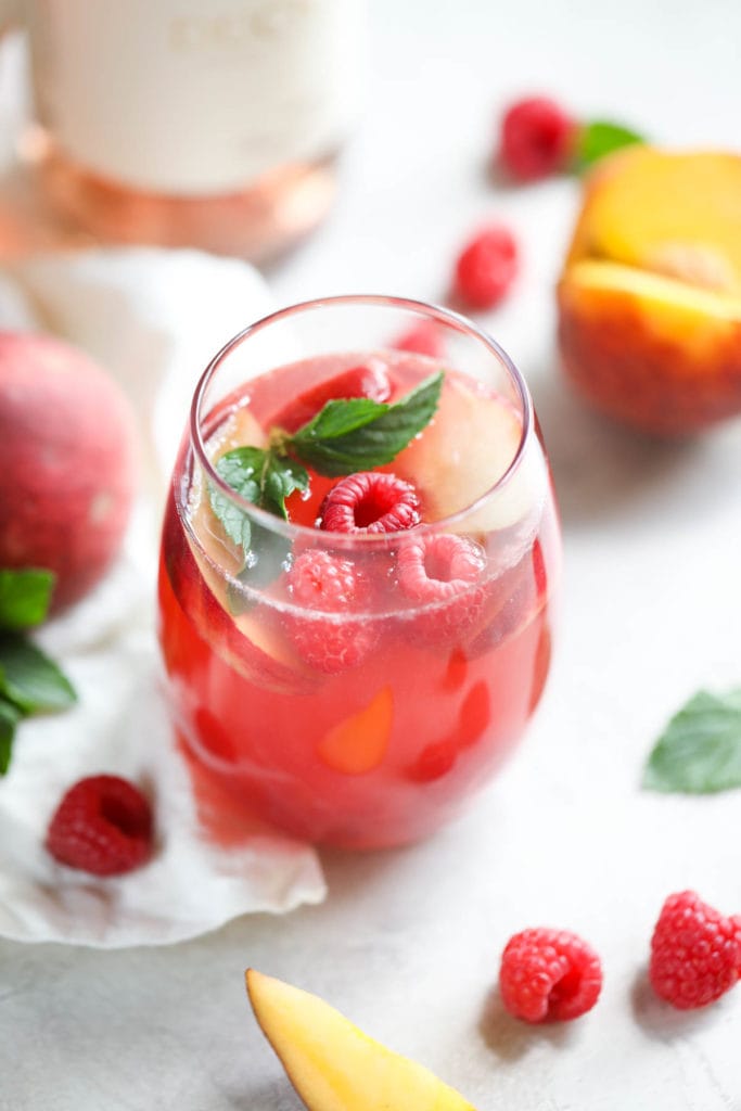 Raspberry peach sangria in a tall glass topped with fresh raspberries and mint leaves