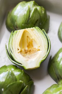 A prepped artichoke brushed with lemon juice and in a baking dish ready for roasting