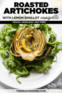 A perfectly roasted artichoke half on a bed of arugula topped with a lemon slice and fresh thyme