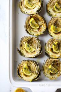 Roasted artichoke halves, cut side up, in a baking dish topped with lemon slices and fresh thyme