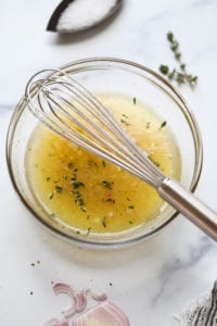 A small bowl filled with lemon shallot vinaigrette, a small whisk resting on the bowl
