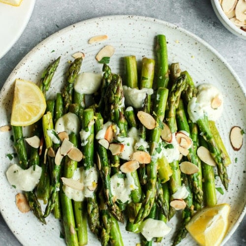 Sautéed asparagus topped with goat cheese sauce and toasted almonds on a speckled plate