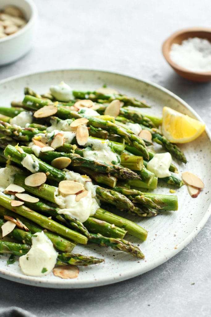 Sautéed Asparagus on a speckled white plate topped with lemon goat cheese sauce and toasted almonds. 