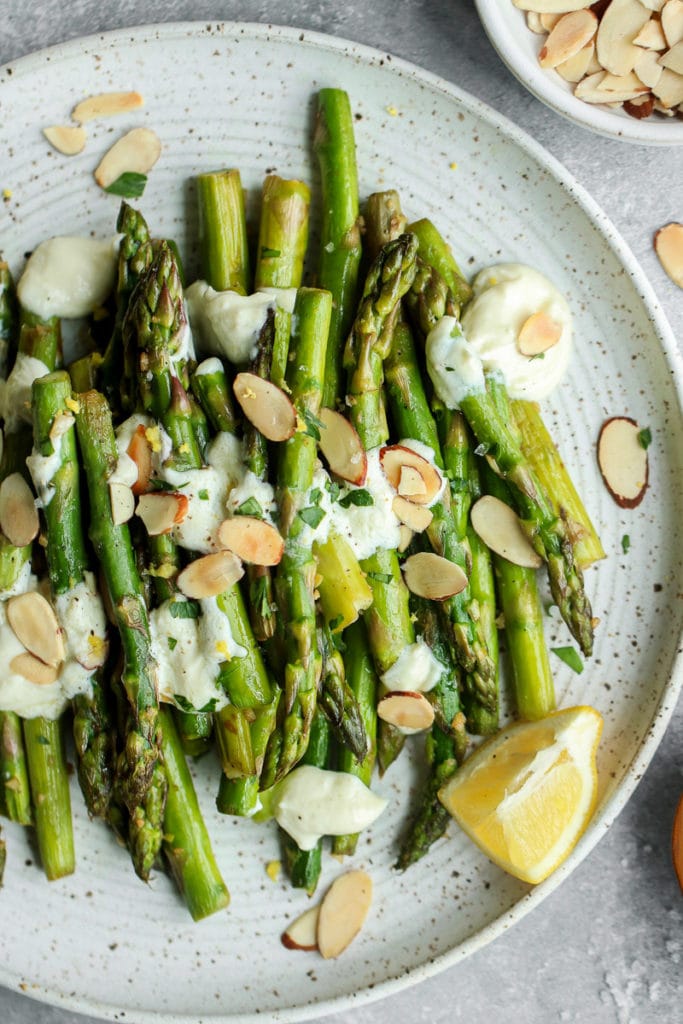 Sautéed Asparagus on a speckled white plate topped with lemon goat cheese sauce and toasted almonds. 