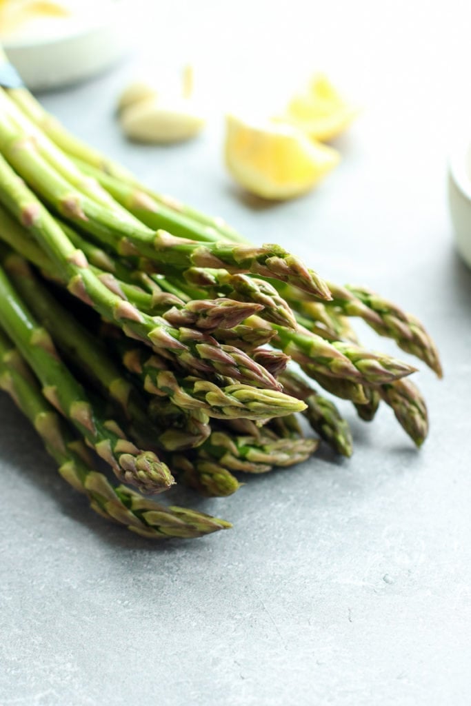 Fresh asparagus spears on grey background with lemon wedges in background.