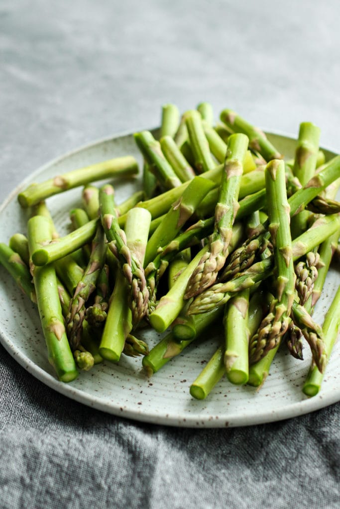 Fresh asparagus spears on a white speckled plate.