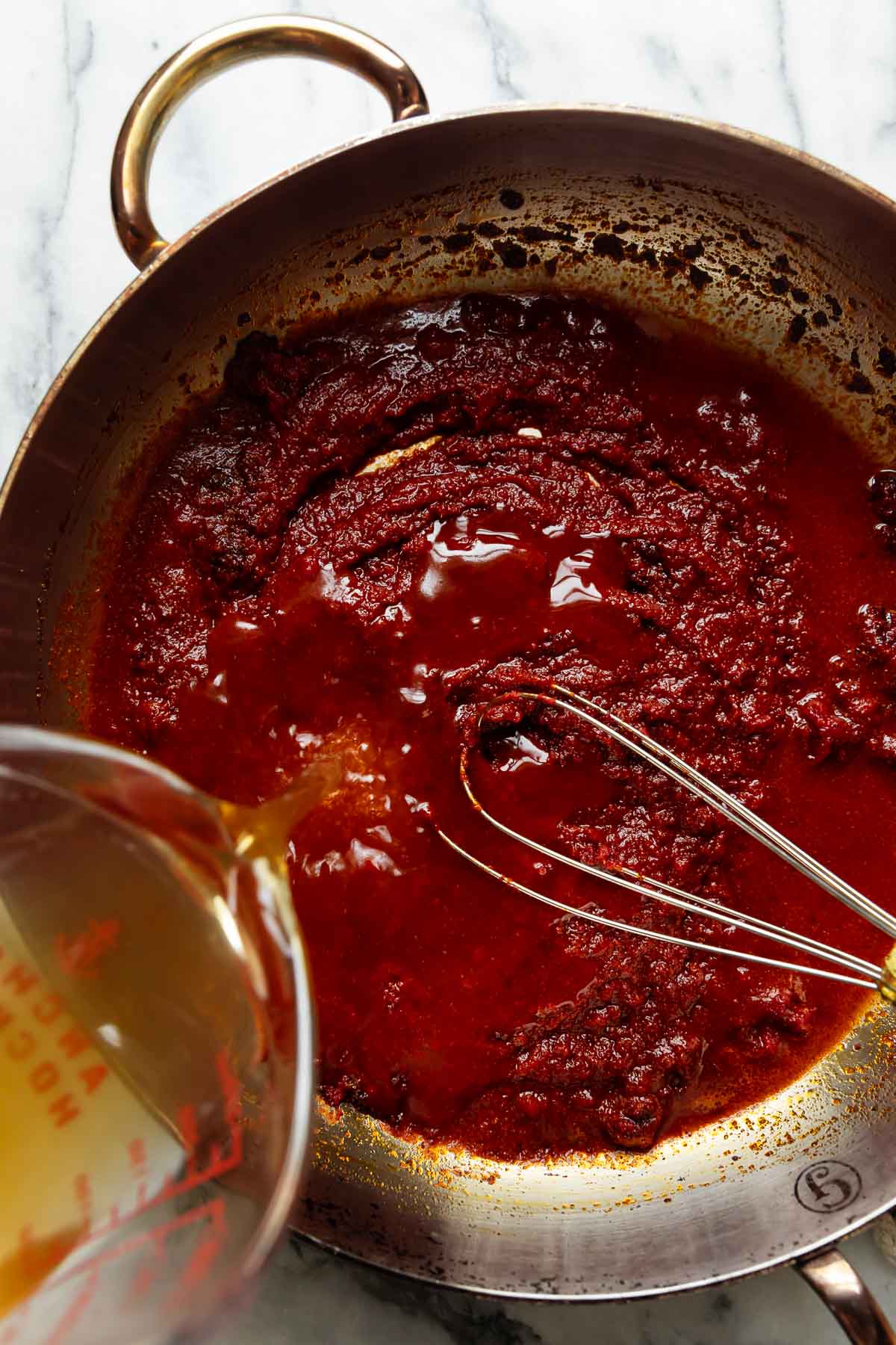 Homemade enchilada sauce being cooked in a skillet with a whisk