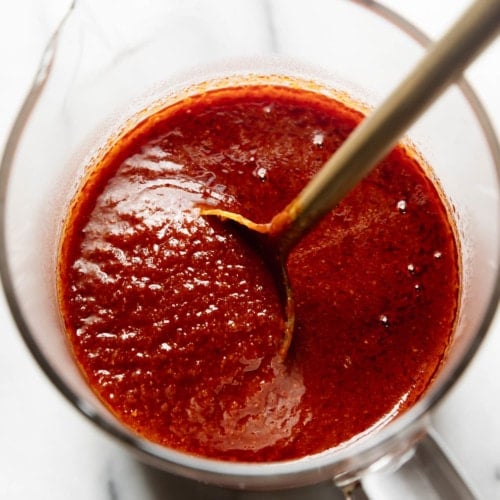 Homemade enchilada sauce in a glass measuring cup with a gold spoon in the sauce