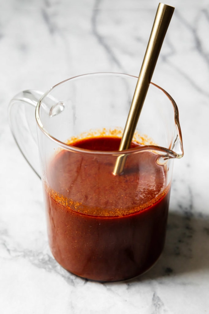 Homemade enchilada sauce in a glass measuring up with a tall gold spoon in the sauce