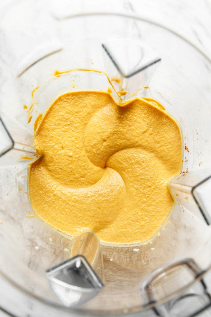 Creamy vegan queso dip perfectly blended in a blender with a swirl appearance from the blending