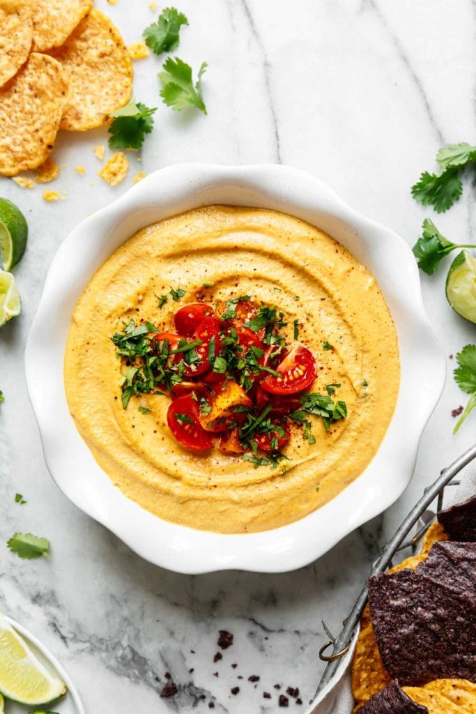 Creamy vegan queso in a scalloped edge white bowl topped with cherry tomatoes and herbs