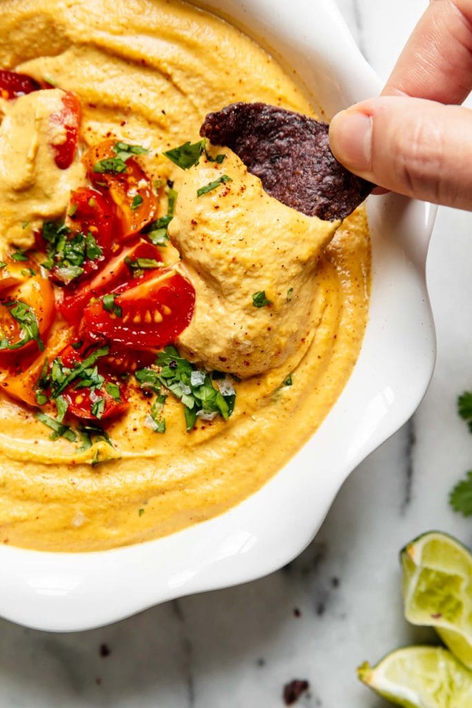 A close up view of vegan queso being dipped with a blue corn chip