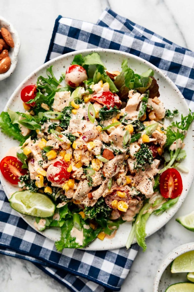 Overhead view of a plate of creamy BBQ Chicken Salad topped with smokey almonds, sweet corn kernels, and grape tomatoes. 