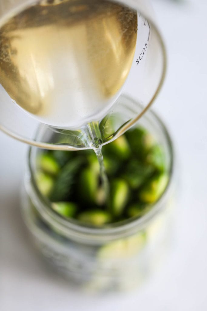 Pickle brine being poured into a mason jar filled with cucumber spears