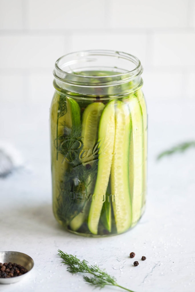 Side view of a mason jar containing fermented pickle spears in brine and dill. 