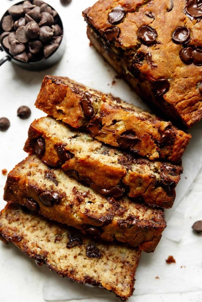 Thick slices of golden brown banana bread studded with chocolate chips next to the cut banana bread loaf