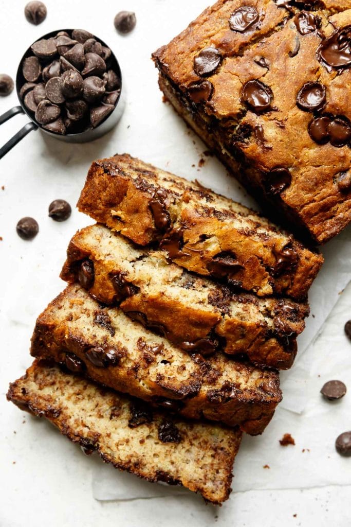 Thick slices of gluten-free banana bread topped with chocolate chips and baked to golden brown cut on a piece of parchment paper