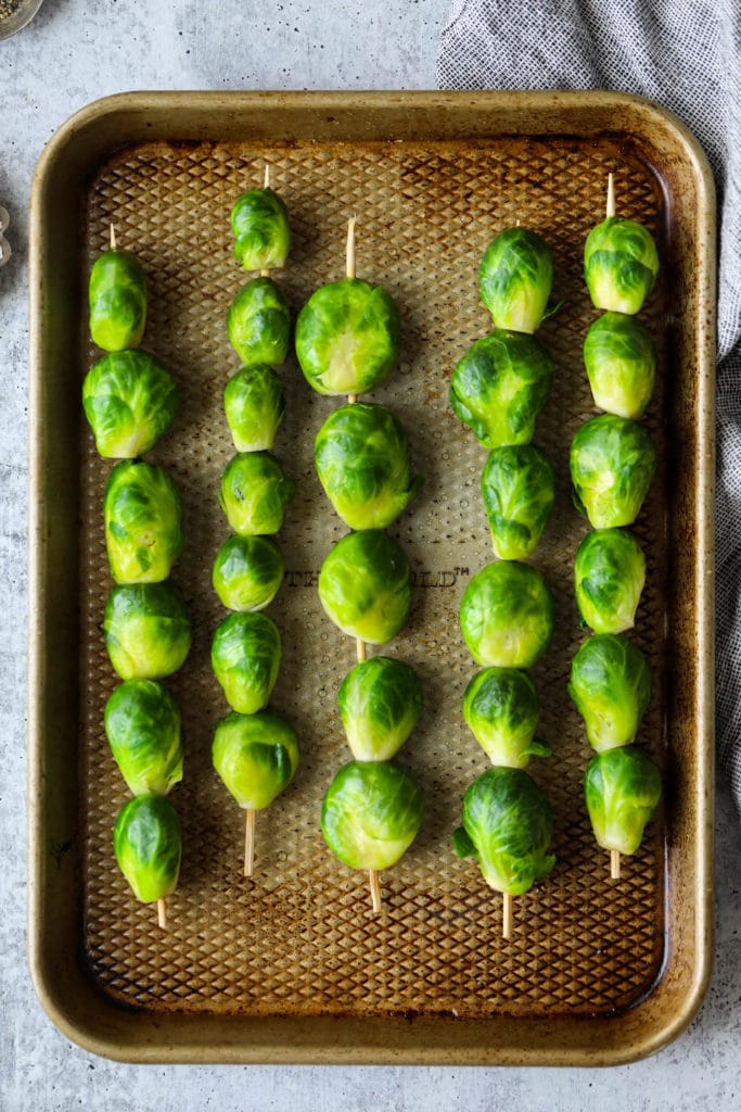 Brussels sprouts threaded on bamboo skewers laying on a baking sheet ready for the grill