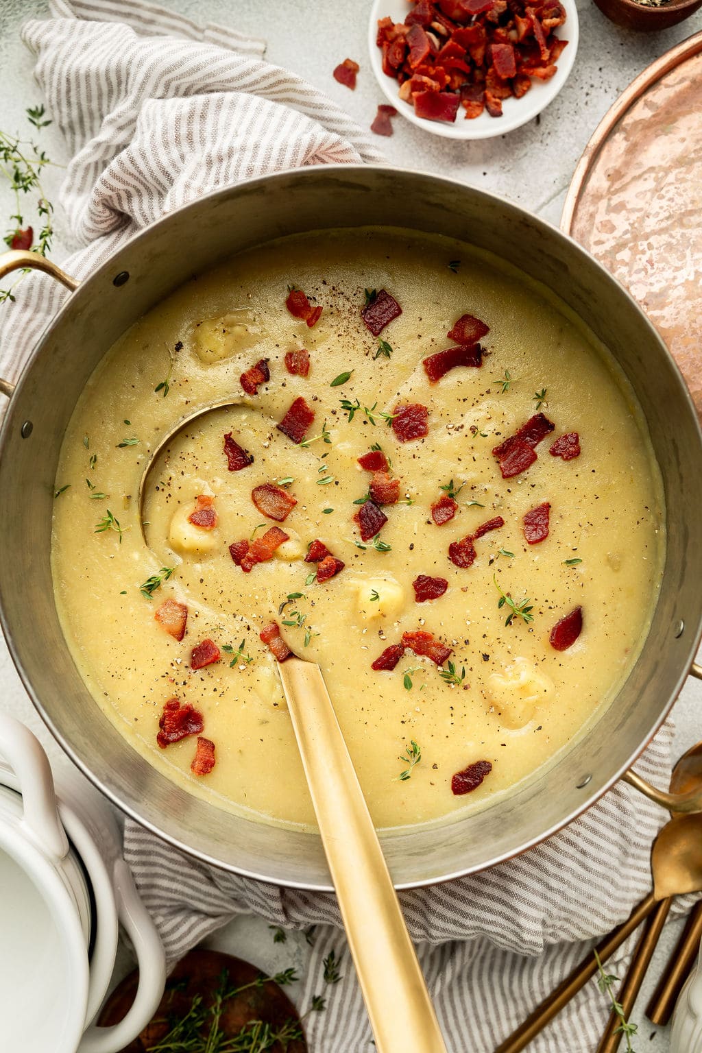 Overhead view of a batch of creamy potato leek soup in large pot with a gold ladle.