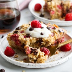 A piece of raspberry baked oatmeal on a speckled plate topped with whipped cream