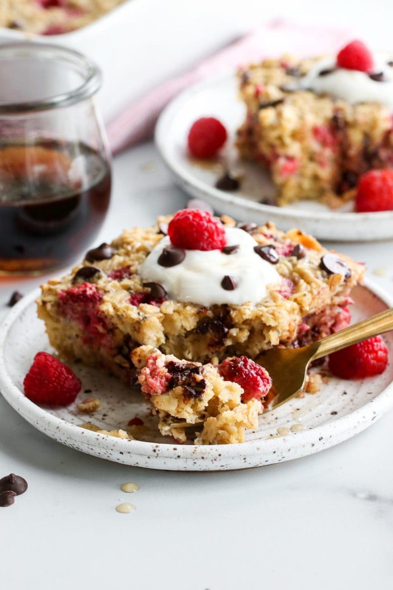 Two plates of raspberry chocolate chip baked oatmeal topped with whipped cream, raspberries, and chocolate chips. 