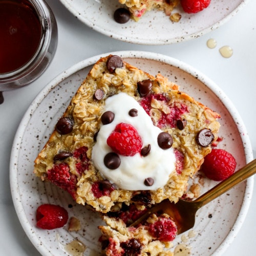 Raspberry baked oatmeal with chocolate chips on a speckled plate with a gold fork and topped with whipped cream